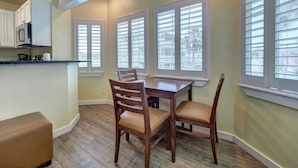 A dining area with a wooden table and chairs, a kitchen with white cabinets, and large windows with blinds. - Seashell Village Resort near the beach with kitchens (Port Aransas)
