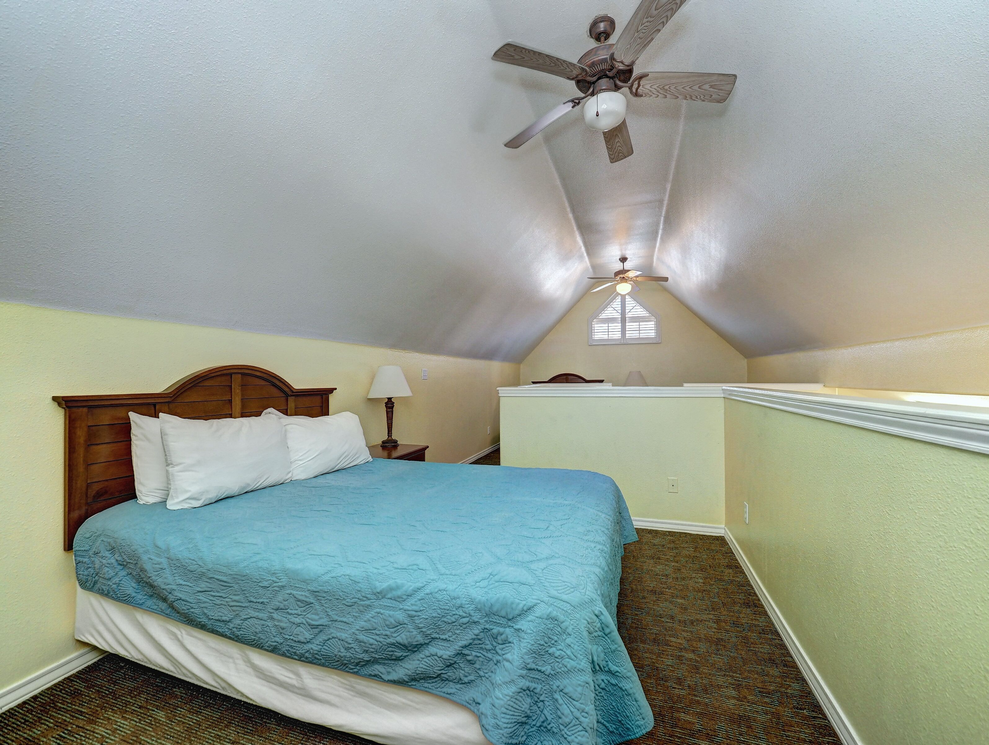 A bedroom with a bed, a nightstand, a lamp, a ceiling fan, and a window.