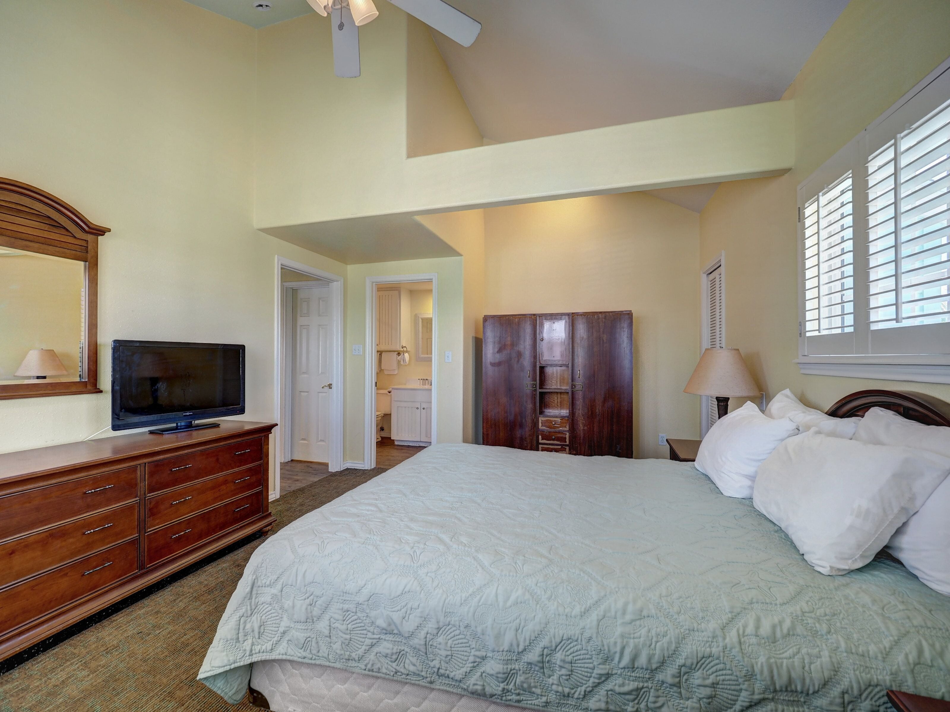 A bedroom with a bed, dresser, television, wardrobe, and a bathroom visible through an open door.
