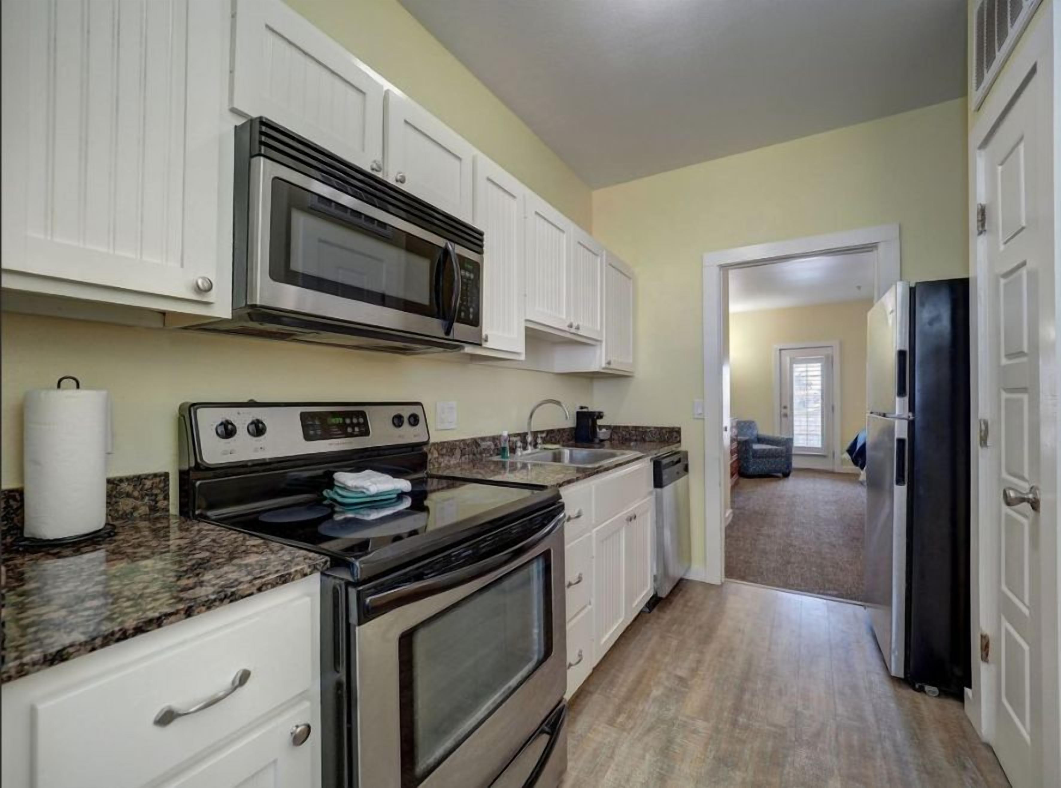 Una cocina con armarios blancos, microondas, estufa y refrigerador.