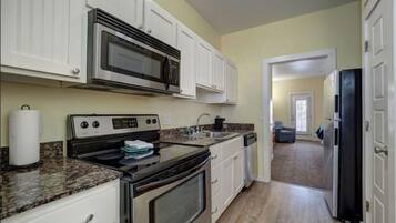 Una cocina con armarios blancos, microondas, estufa y refrigerador.