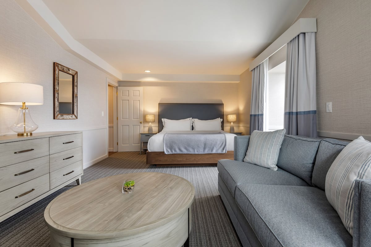 A hotel room with a bed, a sofa, a round coffee table, a dresser, and a mirror.