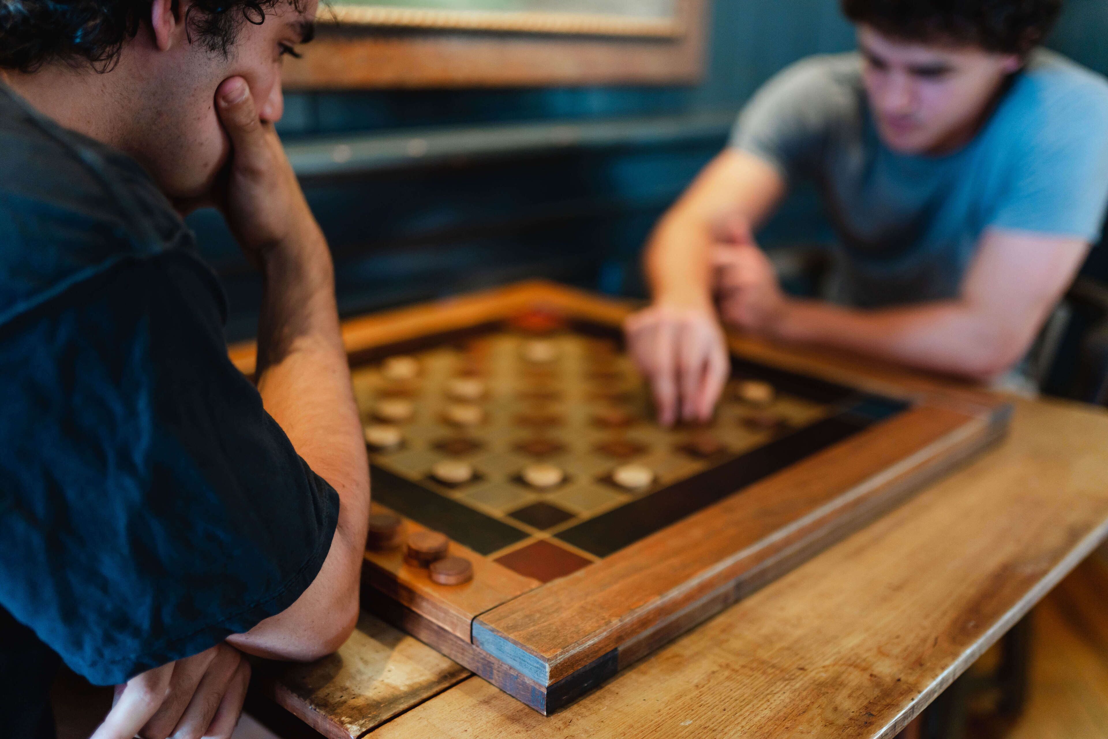 Two people playing a wooden board game at a table.