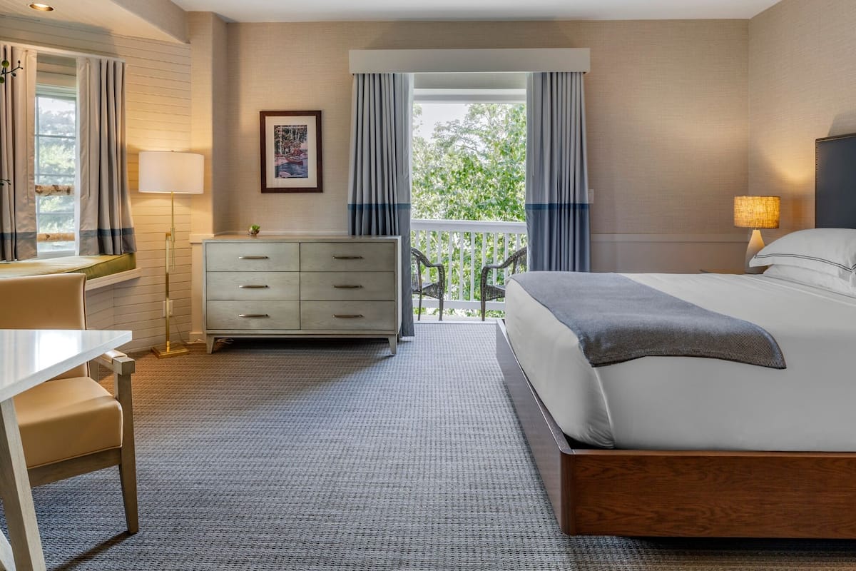A hotel room with a bed, a desk, a dresser, and a balcony with curtains.