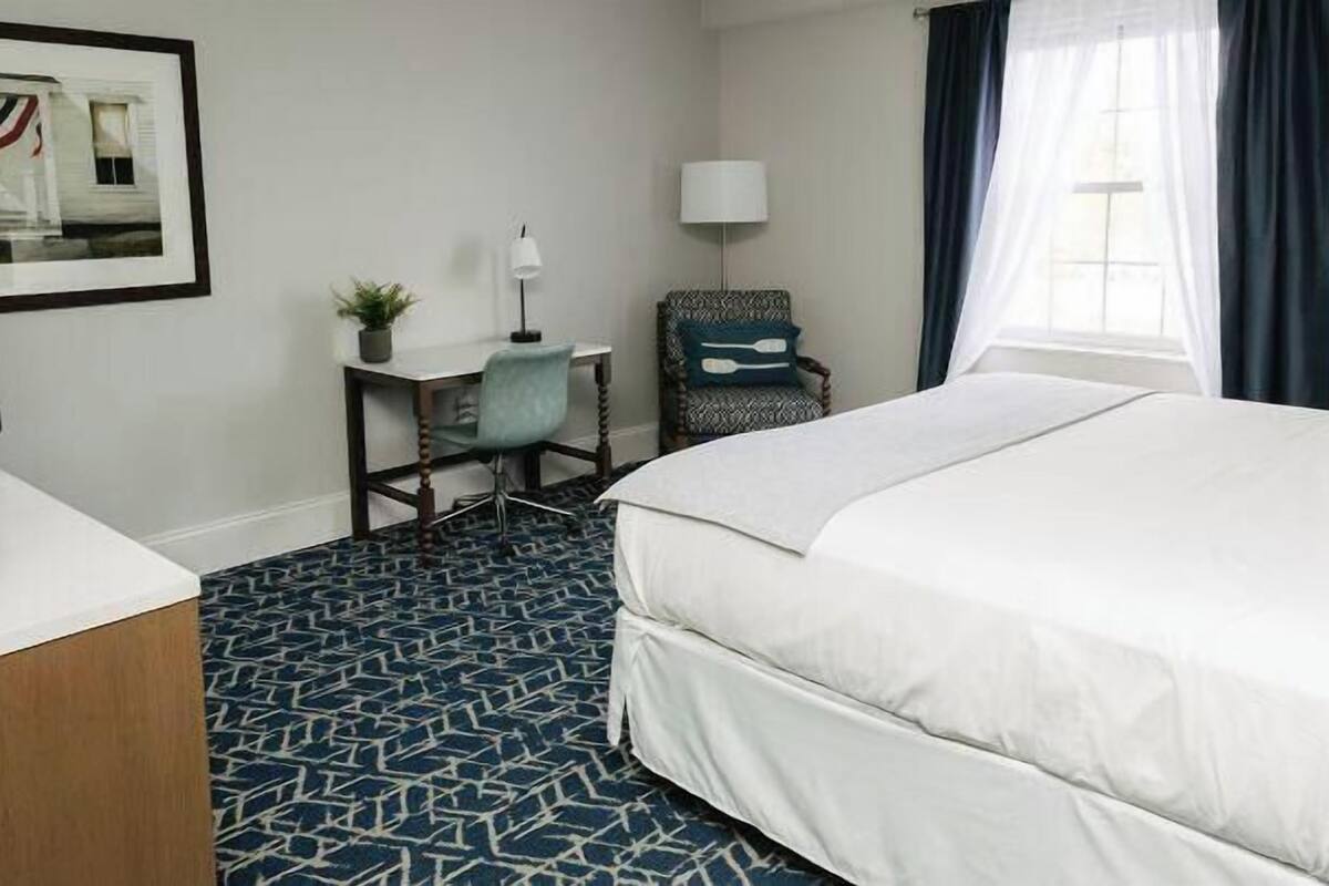 A hotel room with a large bed, a desk with a chair, a television, and a window with curtains.