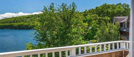 A balcony with a view of a lake and forest, featuring a table with two drinks and a chair.