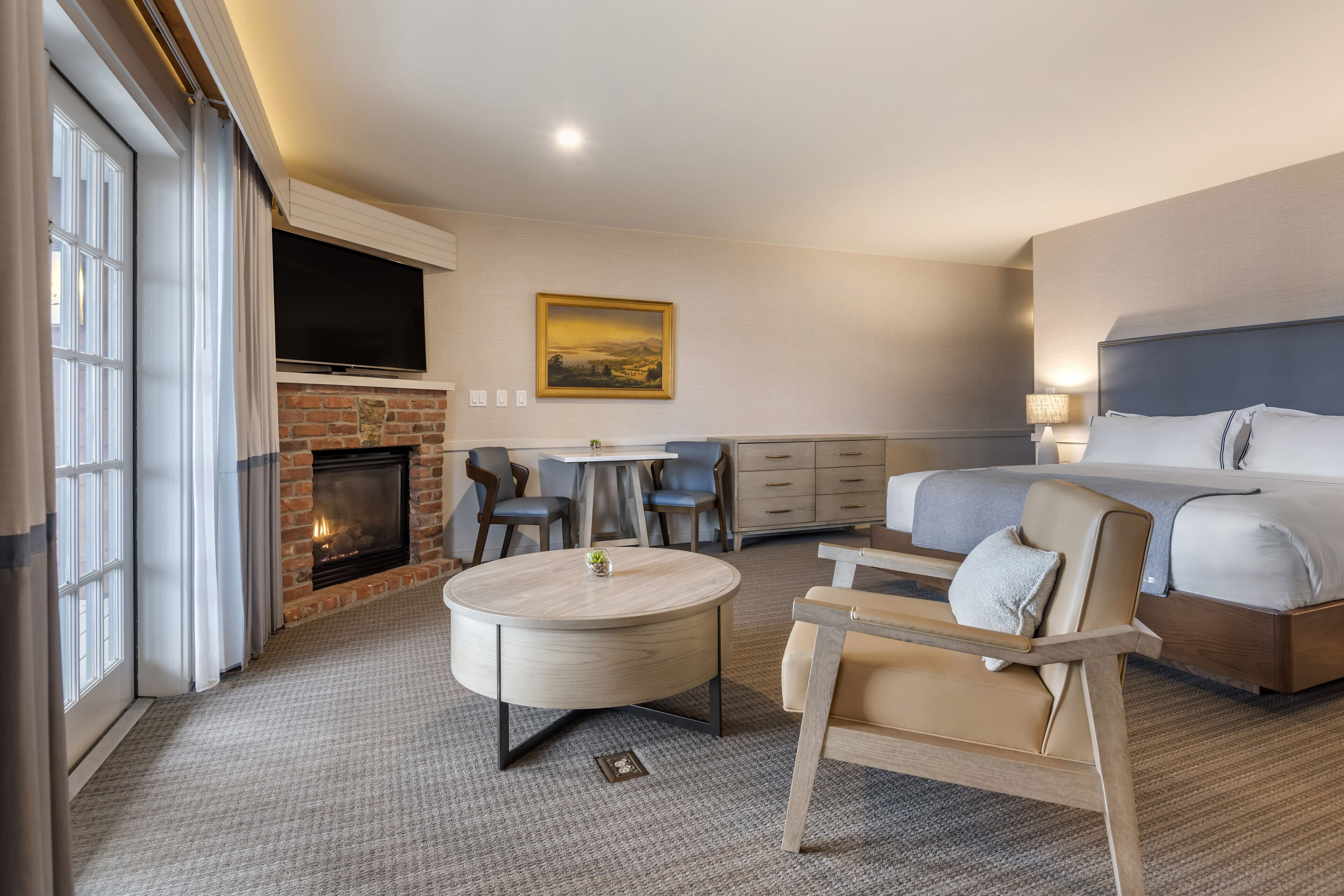 Habitación de hotel con chimenea, televisor montado en la pared, cama, escritorio y una silla.