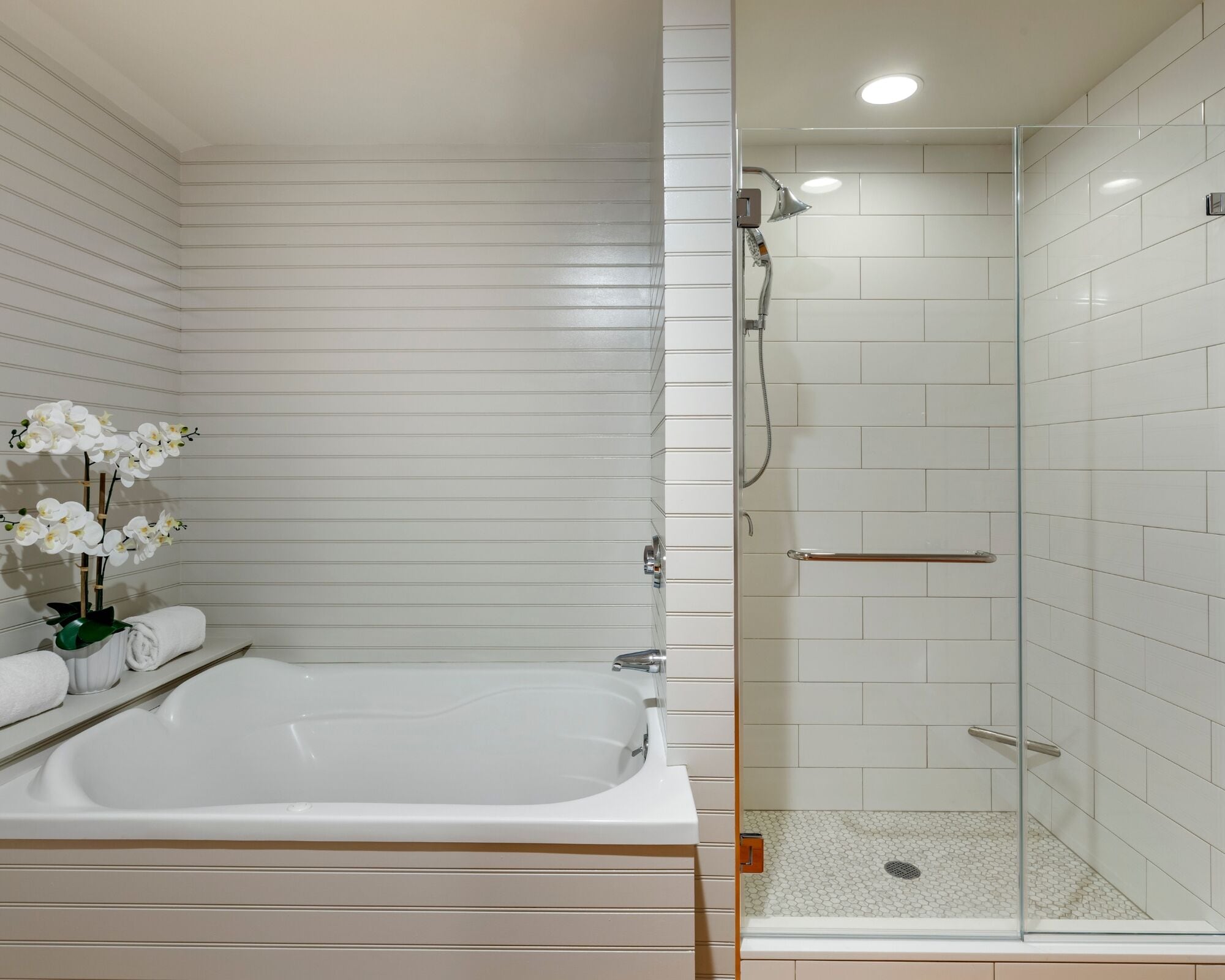 Une salle de bain moderne avec une grande baignoire, une douche à l’italienne et des murs recouverts de carreaux blancs.