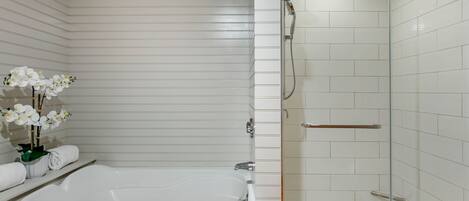 Une salle de bain moderne avec une grande baignoire, une douche à l’italienne et des murs recouverts de carreaux blancs.