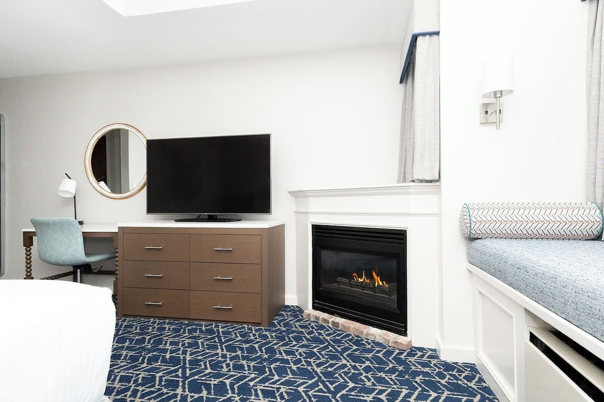A hotel room with a TV, a fireplace, a desk, and a bed.