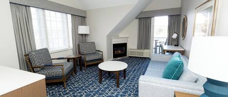 Une chambre d’hôtel avec une cheminée, un canapé, deux fauteuils, une table ronde et un tapis à motifs.