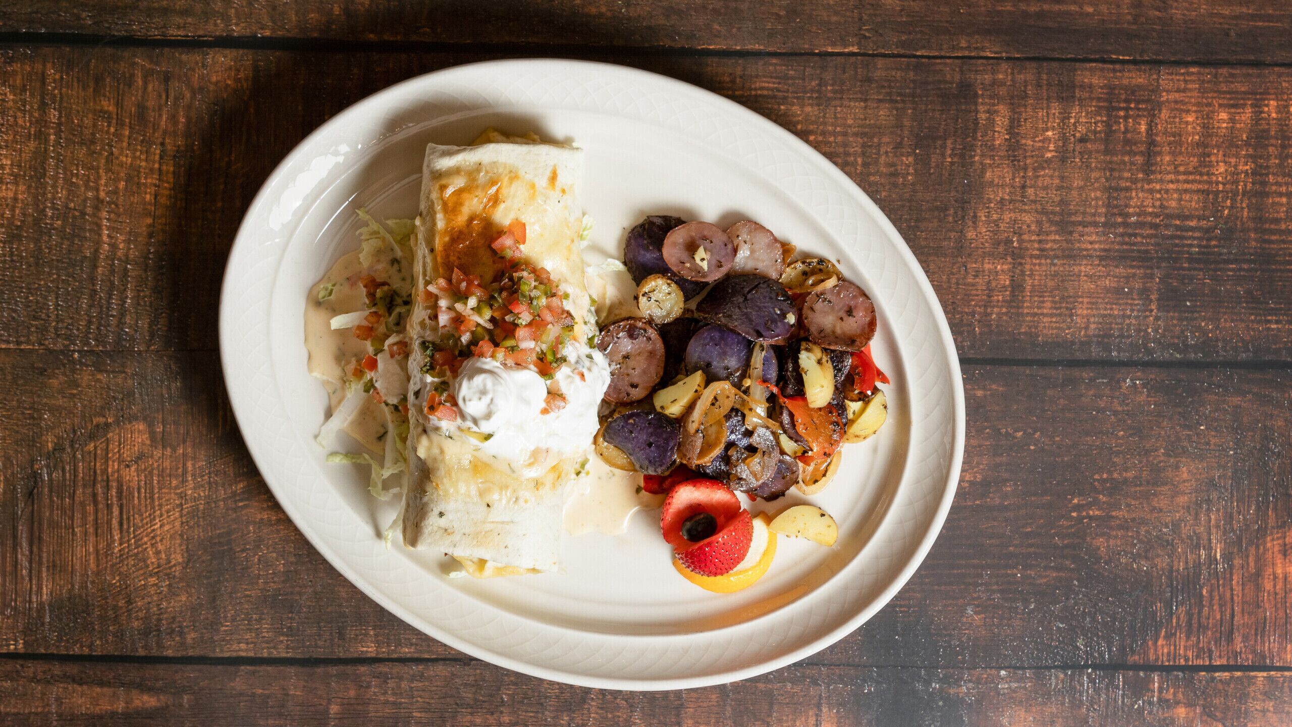 Un plato con un wrap, vegetales asados y una fresa.