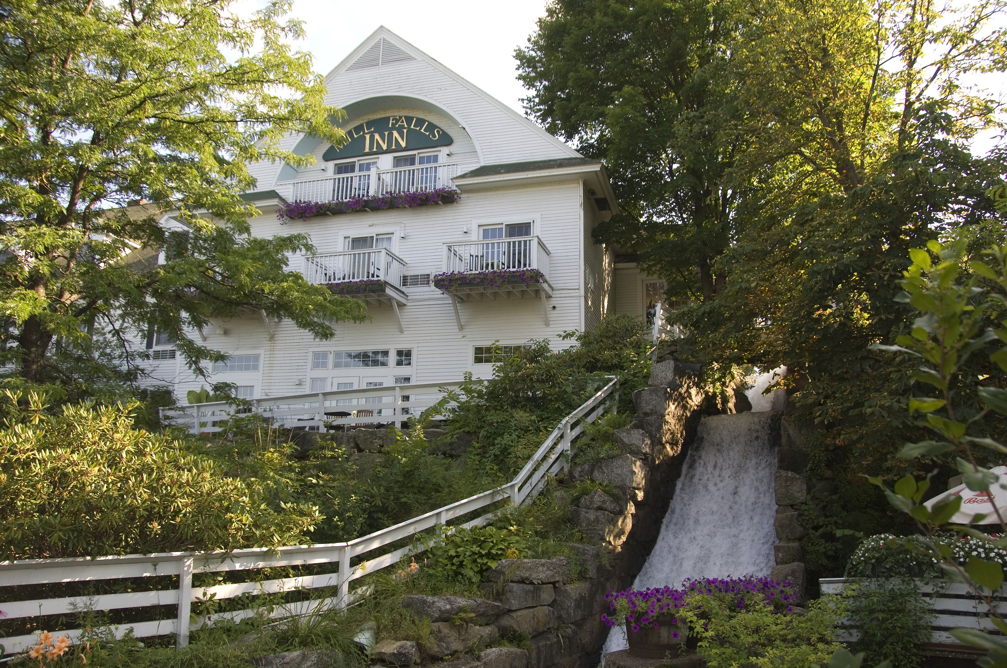 A white building with a sign reading "Hill Falls Inn" and balconies with purple flowers.