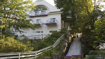 A white building with a sign reading "Hill Falls Inn" and balconies with purple flowers.