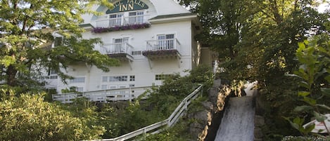 A white building with a sign reading "Hill Falls Inn" and balconies with purple flowers.