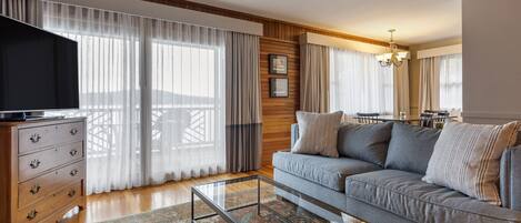 Una sala de estar con un sofá, una mesa de centro de vidrio, un aparador de madera y un televisor.