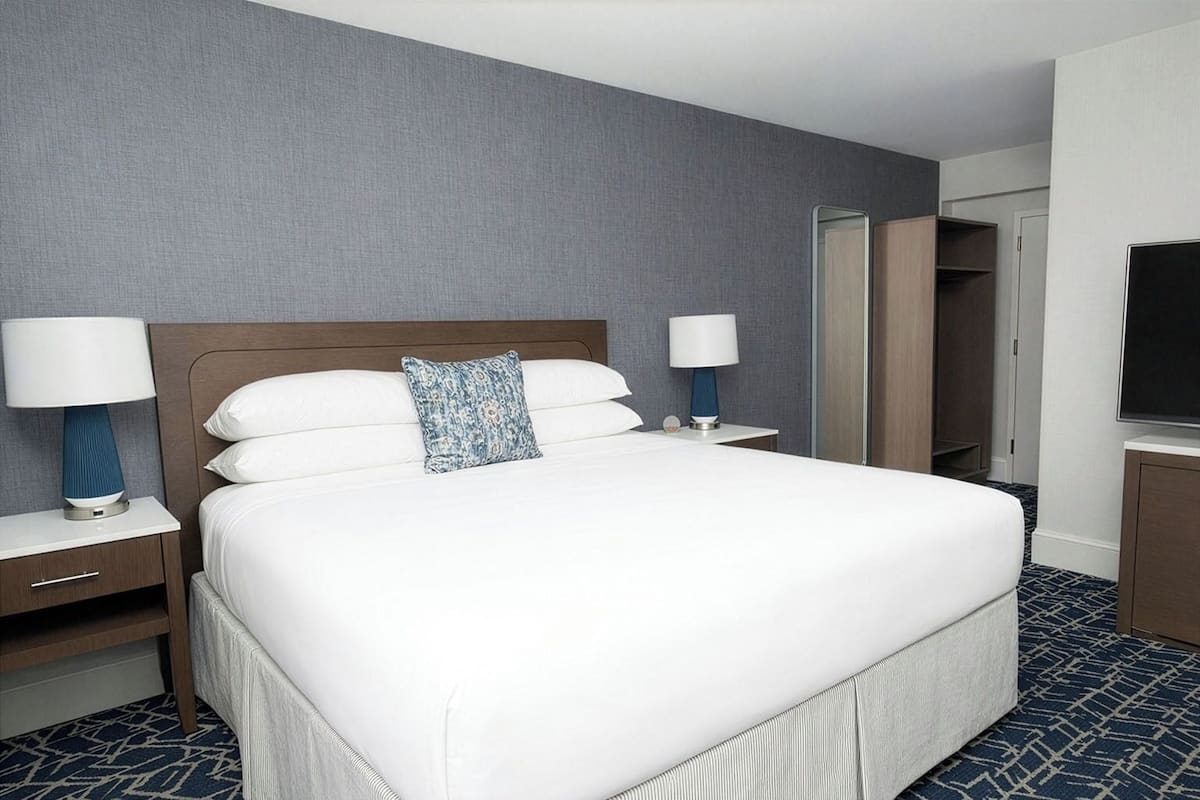 A hotel room with a large bed, two bedside tables with lamps, a wardrobe, and a television.