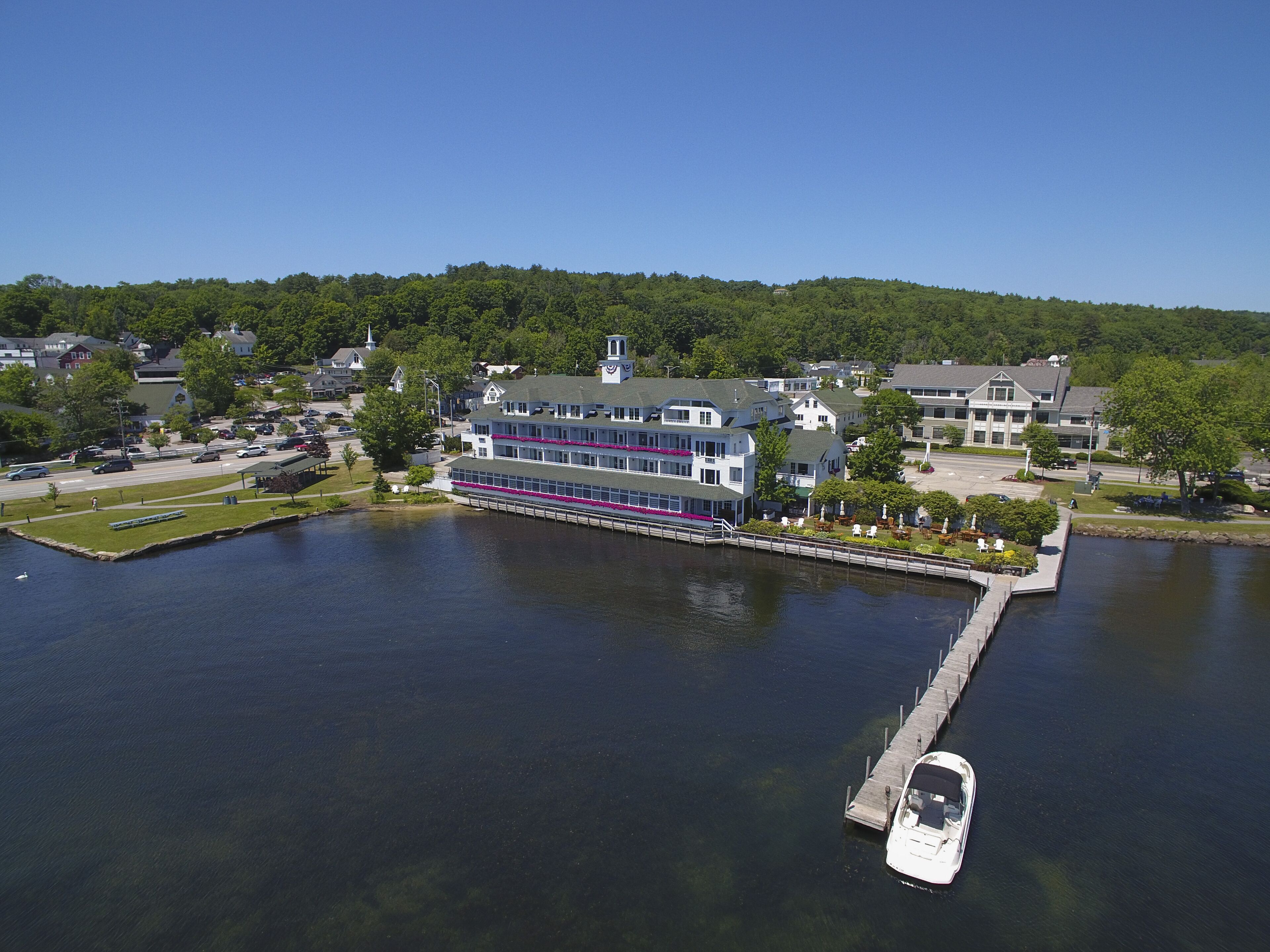 A large, multi-story building with a dock extending into a calm lake, surrounded by greenery and residential buildings.