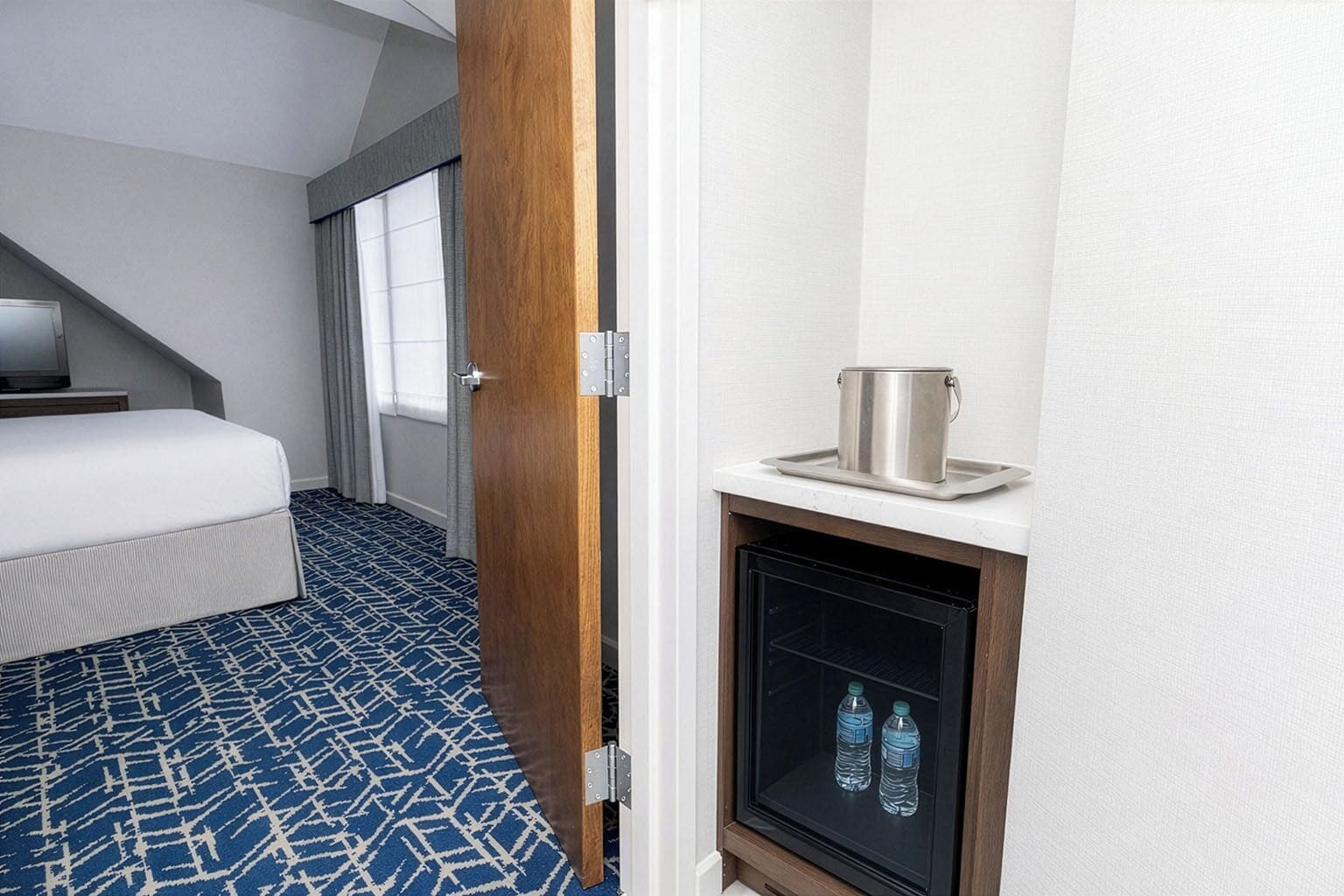 Ett hotellrum med en säng, en minibar och en vattenautomat.