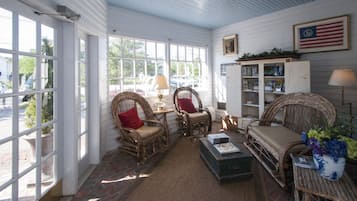A sunlit room with wicker furniture, a bookshelf, and a view of the outside.
