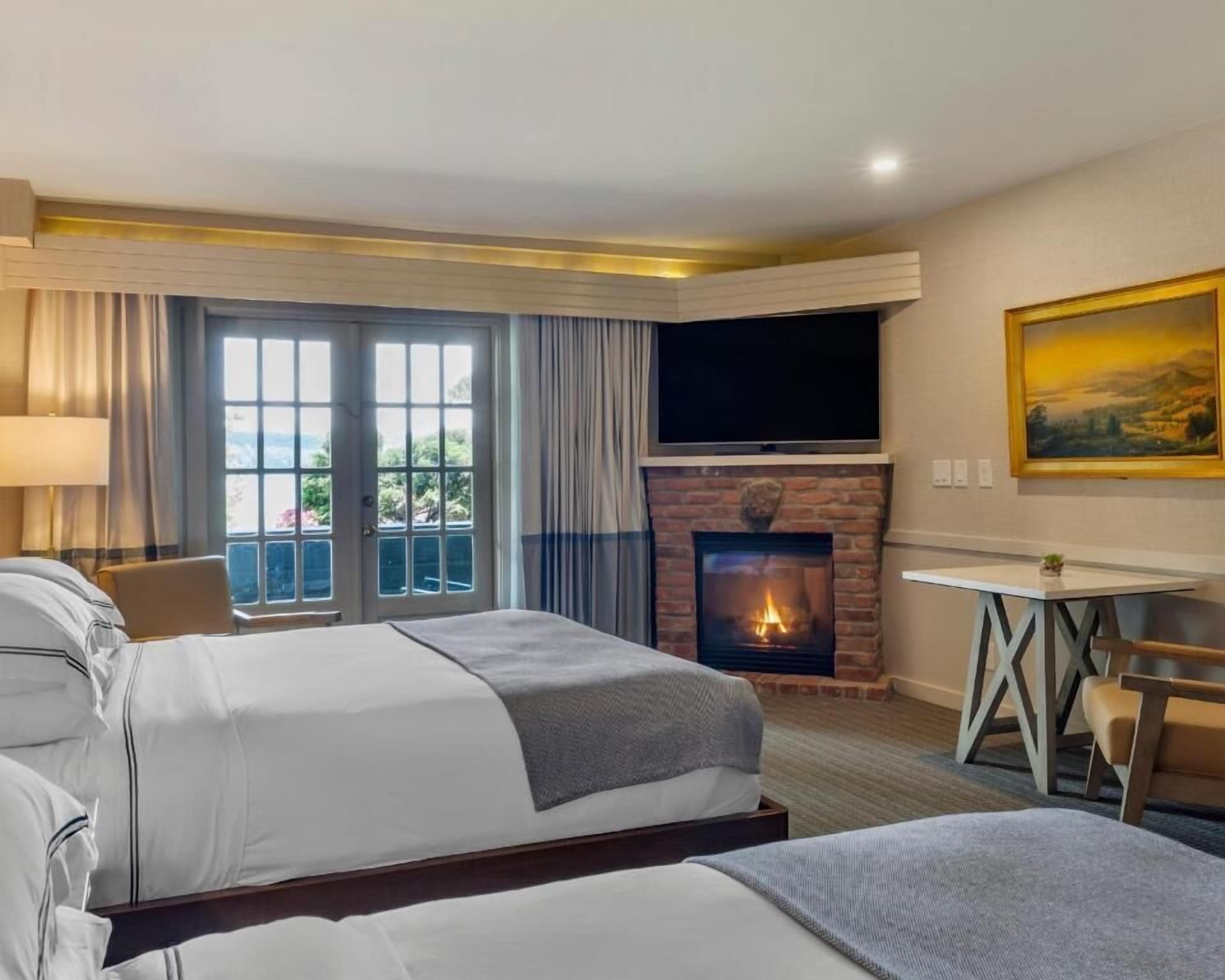 A hotel room with two beds, a fireplace, a TV, and a painting on the wall.