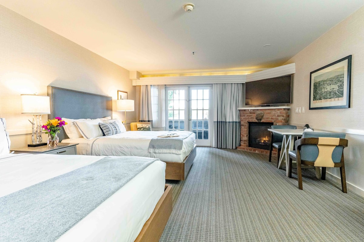 A hotel room with two beds, a fireplace, a TV, and a dining area.