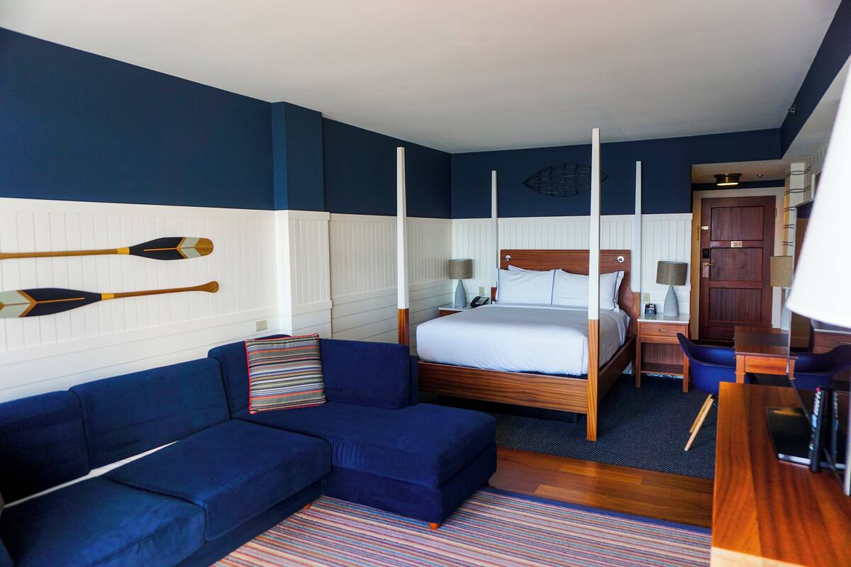 A hotel room with a large bed, a sofa, a desk, and two potted plants.