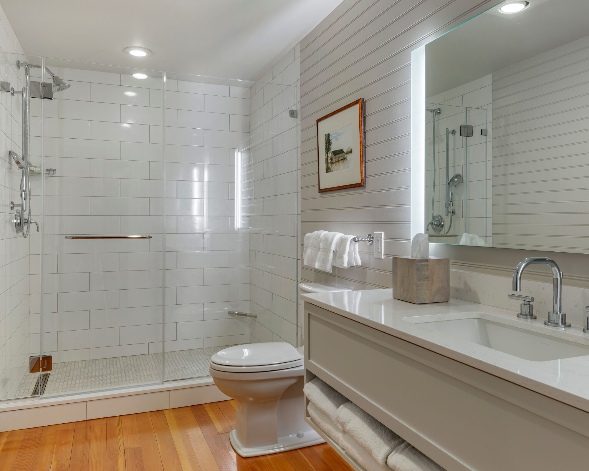 Une salle de bain moderne avec une douche à parois de verre, des toilettes blanches, un meuble-lavabo avec un miroir et un porte-serviettes.