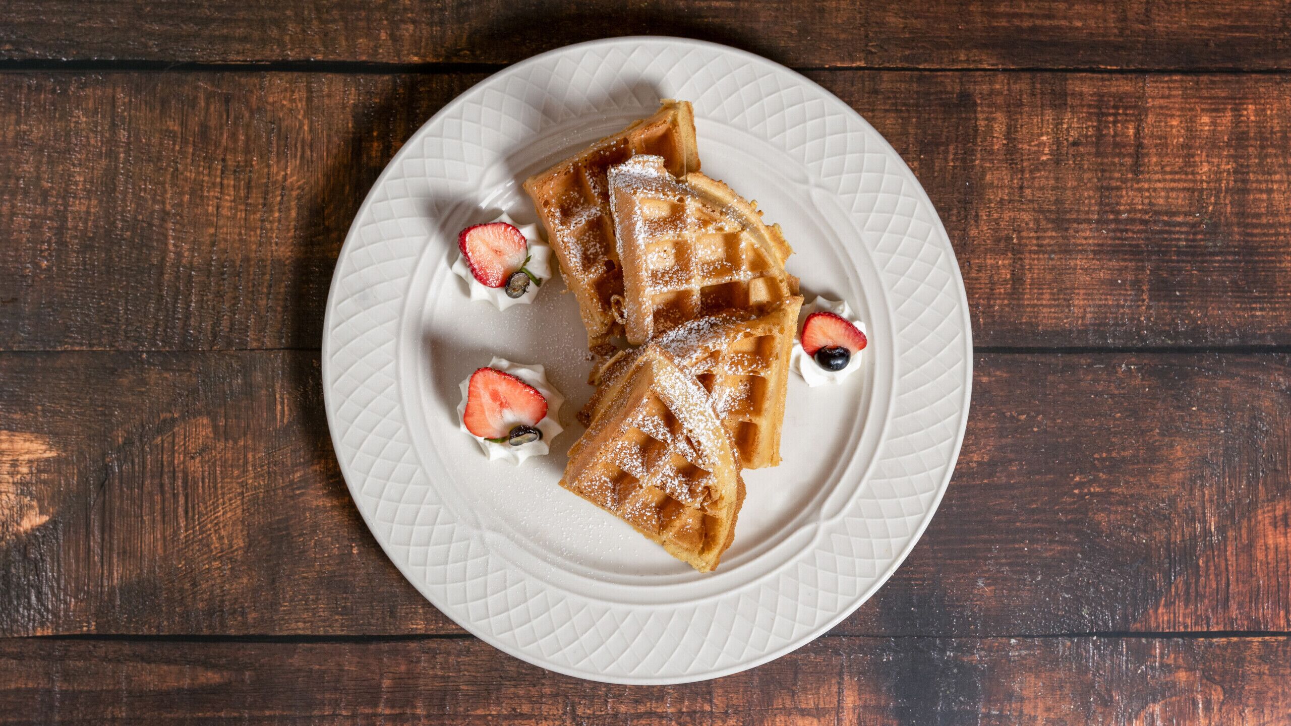 A plate of waffles with strawberries and whipped cream.