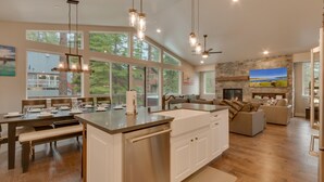A spacious kitchen with a central island, large windows, and a stone fireplace. - Golden Tee, Classic Arcade, Slot Machine, Spa, 7mins to Beach/ Lake, Newly Built – Sierra Escape (South Lake Tahoe)