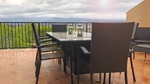 Eine Terrasse mit Tisch und Stühlen, einem Laternen und Blick auf Grünflächen und Berge.