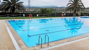 Ein Swimmingpool mit klarem, blauem Wasser, umgeben von Palmen und Blick auf ferne Berge.