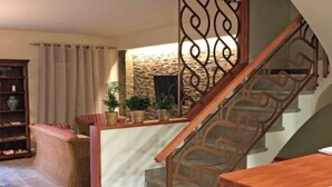Eine Treppe mit Holzgeländer und schmiedeeisernem Geländer führt zu einem Wohnbereich mit Kamin aus Stein, einer Couch und einem Bücherregal.