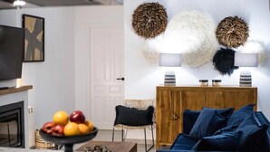 Ein Wohnzimmer mit einem dunkelblauen Sofa, einem Holzkabinett, einer Obstschale und dekorativen, runden Kissen an der Wand.