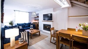Ein modernes Wohnzimmer mit Sofa, Couchtisch und Essbereich, einem Kamin und einem an der Wand montierten Fernseher.