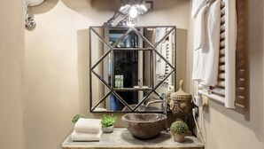 Une salle de bain avec un miroir, un lavabo, une serviette, des plantes en pot et un bol décoratif en pierre.