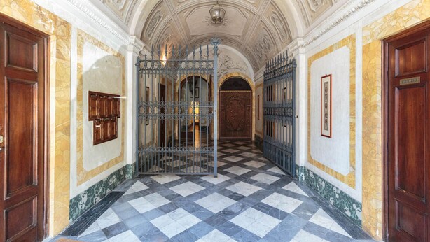 Un couloir doté d’un sol à carreaux, d’un plafond orné et de grilles en métal.