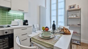 Una cocina moderna con armarios blancos, salpicadero verde y una zona de comedor con mesa para dos.