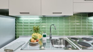Una cocina moderna con armarios blancos, un salpicadero de azulejos verdes, un lavamanos de acero inoxidable y un cuenco de frutas.