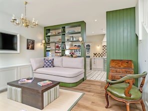 A cozy living room with a sofa, a wooden coffee table, a green upholstered chair, and a bookshelf filled with books and decorative items. - Home Farm Cottage - UK10382 (Glenkindie, near Alford)