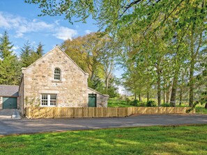 A stone building with a gabled roof, a wooden fence, and a grassy foreground. - Home Farm Cottage - UK10382 (Glenkindie, near Alford)