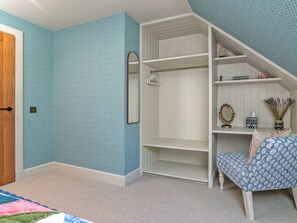 A bedroom with a built-in wardrobe, a mirror, and a seating area with a patterned cushion. - Home Farm Cottage - UK10382 (Glenkindie, near Alford)