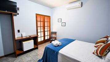 Quarto de hotel compacto com uma cama, uma mesa com computador, uma cadeira e um pequeno frigorífico.