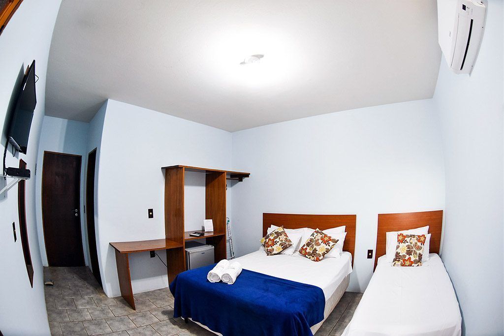A hotel room with two single beds, a desk, a TV mounted on the wall, and a small seating area.