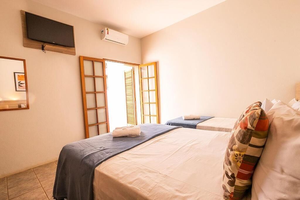 A hotel room with two beds, a television, an air conditioning unit, and a sliding door leading to a balcony.