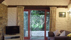 A cozy living room with a stone wall, a television on a white stand, a brown sofa, and a sliding glass door leading to a garden. - 2 bedroom accommodation in Houghton, near Haverfordwest (Houghton, near Haverfordwest)