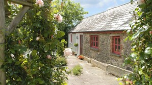 A stone cottage with a tiled patio, surrounded by lush greenery and flowering plants. - 2 bedroom accommodation in Houghton, near Haverfordwest (Houghton, near Haverfordwest)
