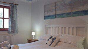 A neatly made bed with pillows, a bedside lamp, and a window with curtains. - 2 bedroom accommodation in Houghton, near Haverfordwest (Houghton, near Haverfordwest)