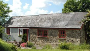 A stone cottage with a sloped roof, red-framed windows, and a small garden area with a bench and potted plants. - 2 bedroom accommodation in Houghton, near Haverfordwest (Houghton, near Haverfordwest)