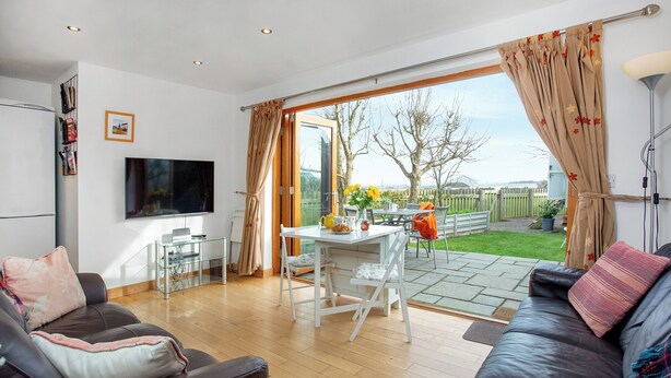 Ein modernes Wohnzimmer mit Sofa, Fernseher, Esstisch mit Stühlen und einer großen Schiebeglastür zum Garten.